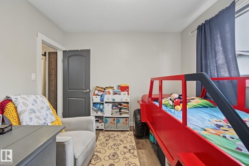 Bedroom featuring light gray wall paint, wood-finish flooring, a two-panel interior door with white trim, and a window with a curtain rod - 3622 115 Avenue, Edmonton, AB 