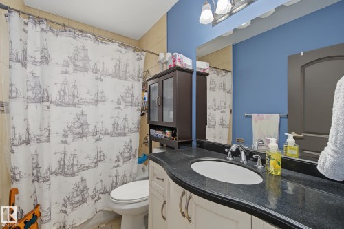 Bathroom featuring a single vanity with a dark countertop and undermount sink, chrome faucet, and integrated mirror - 3622 115 Avenue, Edmonton, AB 