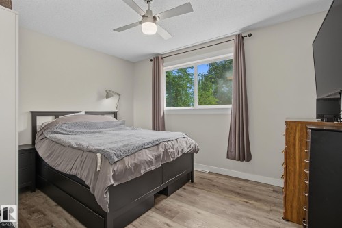 Spacious room featuring wood-finish flooring, a ceiling fan with integrated lighting, and a large window with privacy coverings - 3622 115 Avenue, Edmonton, AB 