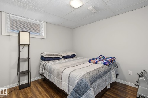 Room featuring wood-finish flooring, a window with blinds, a drop ceiling, white walls, and an overhead light fixture - 3622 115 Avenue, Edmonton, AB 