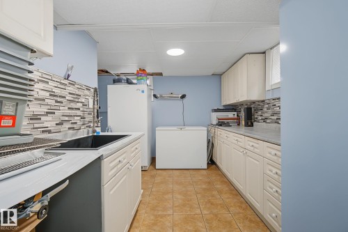 Galley-style utility area featuring white cabinetry, a black undermount sink with a high-arc faucet, and a multi-tone mosaic tile backsplash - 3622 115 Avenue, Edmonton, AB 
