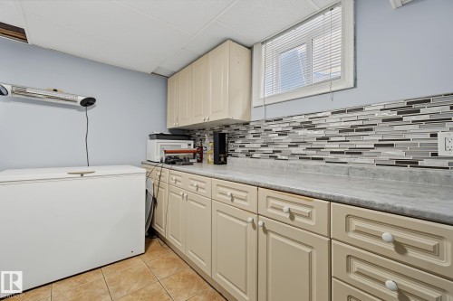 Functional utility area featuring a window, overhead cabinetry, and a full counter with a mosaic tile backsplash - 3622 115 Avenue, Edmonton, AB 
