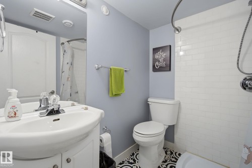 Bathroom featuring a white subway tile shower surround, a vanity with a white basin sink, polished chrome fixtures, and patterned floor tiling - 3622 115 Avenue, Edmonton, AB 