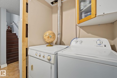 Dedicated laundry area featuring a washer and dryer, an overhead storage cabinet with a wooden frame, and light neutral wall paint - 3622 115 Avenue, Edmonton, AB 
