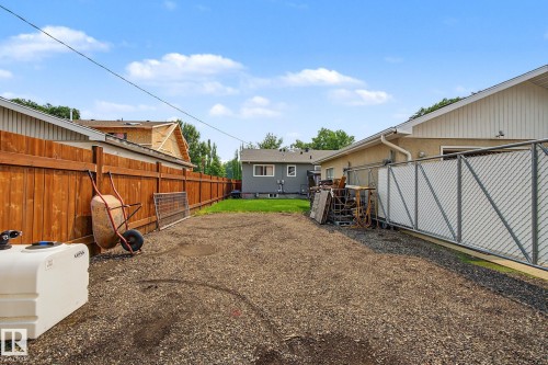 Spacious gravel-covered yard featuring a wood privacy fence and a chain link fence with white privacy screening - 3622 115 Avenue, Edmonton, AB 