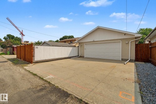 Detached garage with a white overhead door and stucco exterior, featuring a concrete driveway, perimeter wood fencing, and an additional chain-link fence - 3622 115 Avenue, Edmonton, AB 