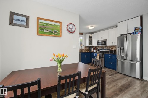 Bright kitchen featuring two-tone cabinetry, stainless steel appliances, a mosaic tile backsplash, and wood-finish flooring - 3622 115 Avenue, Edmonton, AB 