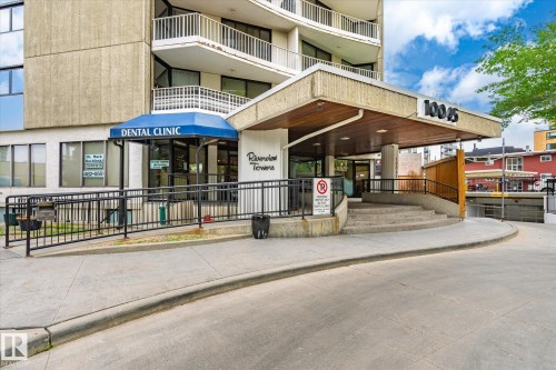 Building facade featuring a prominent main entrance, a covered entryway with a wood-finish soffit, and a distinct building number "10045." The entrance includes a concrete staircase and an adjacent ramp with black metal railings - 503 10045 117 Street, Edmonton, AB 