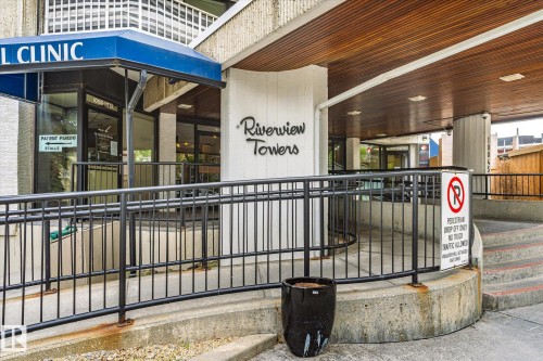 Building entrance featuring an accessible ramp with black metal railings, a covered walkway with wood-finish ceiling panels, and a concrete facade - 503 10045 117 Street, Edmonton, AB 