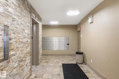 Building hallway featuring a stone-clad wall, elevator access, and a bank of mailboxes - 503 10045 117 Street, Edmonton, AB 