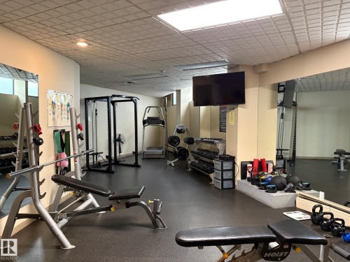 Dedicated fitness center featuring rubber flooring, mirrored walls, recessed lighting, and a wall-mounted display - 503 10045 117 Street, Edmonton, AB 