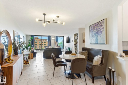 Open-concept living area featuring tile flooring, a contemporary ceiling light fixture, a full wall of windows, and built-in shelving - 503 10045 117 Street, Edmonton, AB 