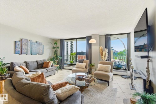 Living area featuring expansive windows, tile flooring, light-toned wall finishes, and balcony access - 503 10045 117 Street, Edmonton, AB 