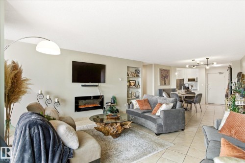 Open-concept living space featuring an electric fireplace with a wall-mounted display, built-in shelving, and tile flooring - 503 10045 117 Street, Edmonton, AB 