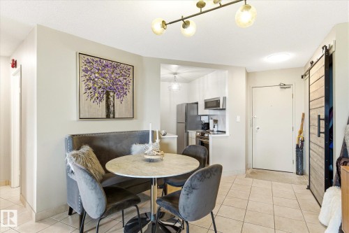 Dining area featuring tile flooring, a modern chandelier, and an open pass-through to the kitchen with stainless steel appliances - 503 10045 117 Street, Edmonton, AB 