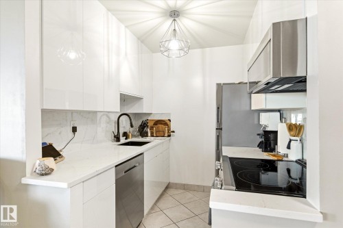 Modern kitchen featuring white high-gloss cabinetry, white countertop, a black sink with a matte black faucet, and stainless steel appliances - 503 10045 117 Street, Edmonton, AB 