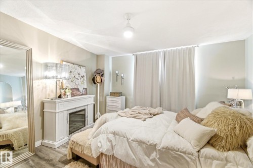 Spacious room featuring wood-finish flooring, a decorative fireplace with a mantel, and light-colored walls - 503 10045 117 Street, Edmonton, AB 