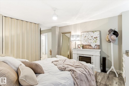 White fireplace mantel featuring a dark firebox, wood-finish flooring, light neutral wall paint, and a ceiling fan with integrated lighting - 503 10045 117 Street, Edmonton, AB 