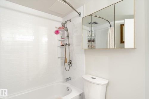 Bright bathroom featuring a white bathtub with subway tile surround, a chrome shower fixture, and a mirrored medicine cabinet - 503 10045 117 Street, Edmonton, AB 