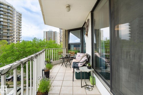 Expansive balcony featuring a white railing, square tile flooring, a large sliding glass door, and surrounding architectural structures - 503 10045 117 Street, Edmonton, AB 