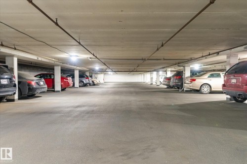 Underground parking garage featuring concrete flooring and ceiling, multiple parking spaces, and overhead lighting fixtures - 503 10045 117 Street, Edmonton, AB 