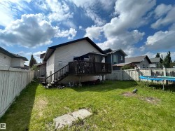 Backyard featuring a wooden deck with a staircase, vinyl siding, and a partial wooden privacy fence - 