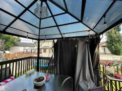 Deck area featuring a gazebo with a corrugated translucent roof, integrated lighting, and privacy curtains - 