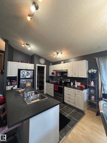 Kitchen featuring white cabinetry with dark hardware, dark countertops, dual basin stainless steel sink, stainless steel range, and track lighting - 17 Willowby Close, Stony Plain, AB 