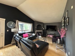 Living area featuring light wood-finish flooring, a vaulted ceiling, a large window, a fireplace with an arched niche, and a white door with trim - 