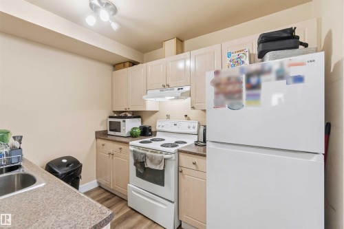 Kitchen featuring light wood-finish cabinetry, speckled countertops, stainless steel sink, and wood-finish flooring - 17118 108 Street, Edmonton, AB 