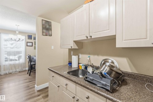 Kitchen area featuring cream-colored cabinetry with silver-tone hardware, a double basin stainless steel sink, and speckled countertops - 17118 108 Street, Edmonton, AB 