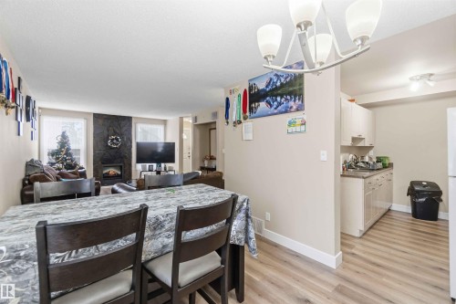 Open-concept living area with wood-finish flooring, a contemporary chandelier, and a stone-clad fireplace - 17118 108 Street, Edmonton, AB 