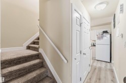 Carpeted staircase with white trim, wood-finish flooring, white paneled doors, and a partial view of a kitchen area with white cabinetry and appliances - 