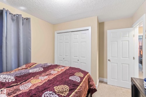 Carpeted bedroom featuring neutral wall tones, white bi-fold closet doors, a white paneled interior door, recessed lighting, and a textured ceiling - 17118 108 Street, Edmonton, AB 