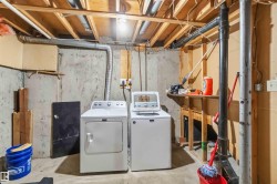 Basement laundry area featuring concrete walls, exposed ceiling joists, and a utility sink - 