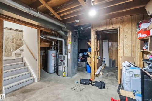 Basement utility area featuring a hot water heater, furnace, exposed ceiling joists, concrete flooring, and wood paneling - 17118 108 Street, Edmonton, AB 