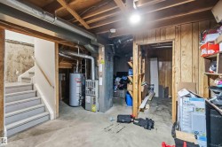 Basement utility area featuring a hot water heater, furnace, exposed ceiling joists, concrete flooring, and wood paneling - 
