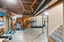 Unfinished basement with concrete flooring, exposed ceiling joists, and a partial wood-paneled wall - 