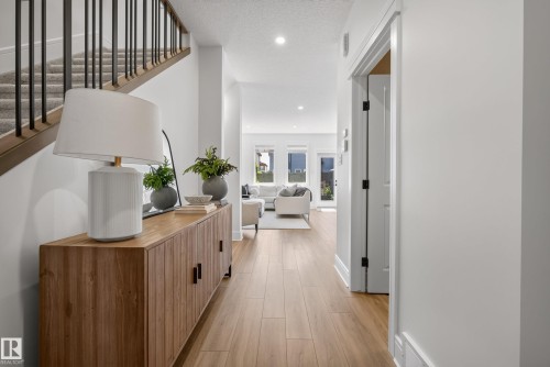 Entryway featuring wood-finish flooring, a contemporary wood console cabinet, and a staircase with metal balusters and carpeted treads - 20907 131 Avenue, Edmonton, AB 