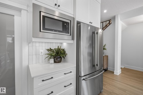 Kitchen area featuring white cabinetry with black hardware, stainless steel appliances, a built-in microwave, and a white tile backsplash - 20907 131 Avenue, Edmonton, AB 