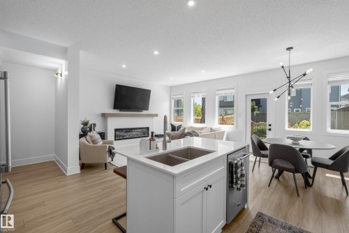 Open-concept living space featuring wood-finish flooring, a kitchen island with an undermount sink, a built-in fireplace with a mantel, recessed lighting, and multiple windows - 20907 131 Avenue, Edmonton, AB 