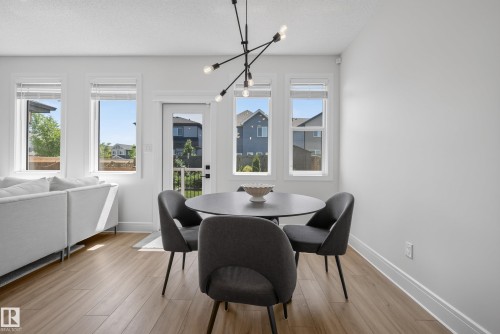 Open-concept dining area featuring wood-finish flooring, a contemporary chandelier, multiple windows, and a glass-paneled door - 20907 131 Avenue, Edmonton, AB 