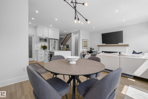Open-concept living space featuring wood-finish flooring, recessed lighting, a modern sputnik chandelier, and a fireplace with a wood mantle - 20907 131 Avenue, Edmonton, AB 