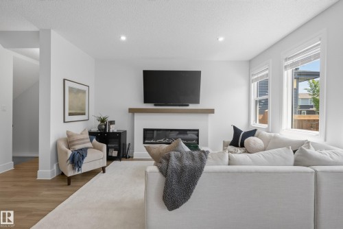 Bright living area featuring a modern electric fireplace with a wood-finish mantel, recessed lighting, and expansive windows - 20907 131 Avenue, Edmonton, AB 