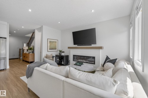 Living area featuring a modern linear fireplace with a wood mantle, recessed lighting, and wood-finish flooring - 20907 131 Avenue, Edmonton, AB 