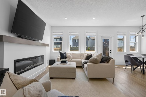 Open-concept living space featuring a linear fireplace with a wood-finish mantel, recessed lighting, multiple large windows, and light wood-finish flooring - 20907 131 Avenue, Edmonton, AB 