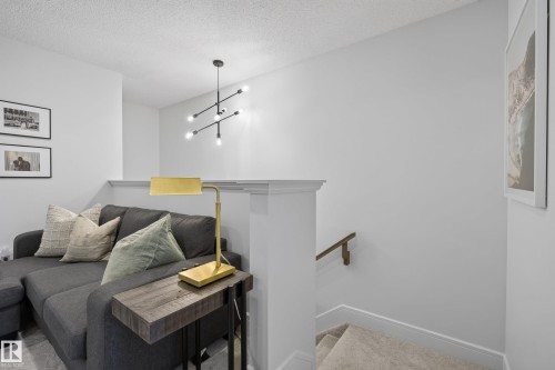 Open loft space featuring white walls, a contemporary black chandelier, a half-wall partition, and carpeted stairs with a wooden handrail - 20907 131 Avenue, Edmonton, AB 
