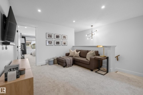 Carpeted upper-level landing featuring a contemporary chandelier, recessed lighting, and a white painted banister - 20907 131 Avenue, Edmonton, AB 