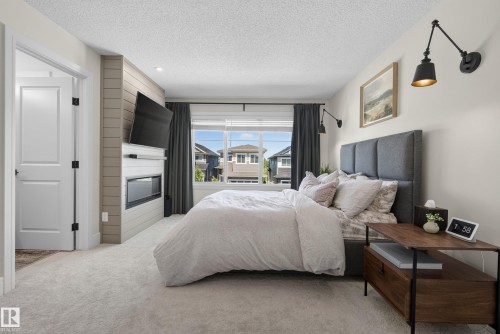 Carpeted bedroom featuring a built-in fireplace, large window with dark drapes, and an upholstered headboard - 20907 131 Avenue, Edmonton, AB 