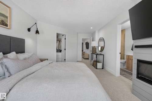 Bedroom featuring neutral carpeting, a shiplap fireplace surround with a black electric fireplace, and a wall-mounted swing-arm sconce - 20907 131 Avenue, Edmonton, AB 